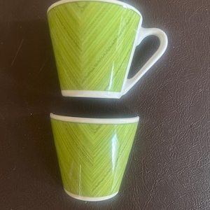 May include: Two green teacups with a white rim and handle. The cups have a chevron pattern in a bright green color. One cup is whole, and the other is broken in half.