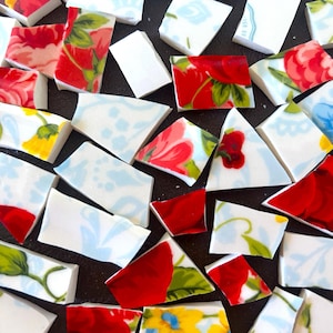 May include: A collection of broken ceramic pieces with floral patterns in red, yellow, and blue. The fragments vary in size and shape, with some featuring solid red sections. The pieces are scattered on a dark surface.