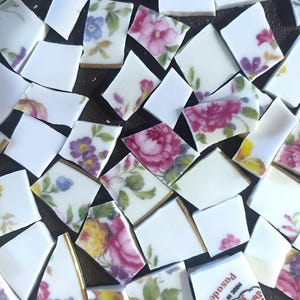 May include: Scattered pieces of broken porcelain with floral patterns in pink, purple, yellow, and blue. The fragments have gold trim and are on a dark surface. Some pieces are plain white.