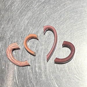 May include: Four curved, semi-circular ceramic pieces in varying shades of pink and brown. One piece has a textured, speckled surface, while the other three have a smooth, glossy finish. The shapes range from short arcs to a longer, slender curve.
