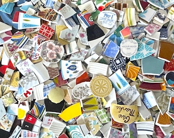 May include: A collection of colorful, broken ceramic tiles with various patterns and designs. The tiles are mostly white with blue, red, and green accents. Some tiles have text, including "Give Thanks" and "Sango Anchor Meade".
