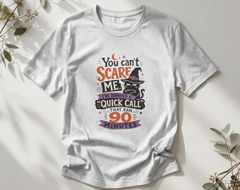 May include: A light gray short-sleeve t-shirt featuring a graphic of a black cat wearing a witch hat. The text reads: You can't SCARE ME. I'VE SURVIVED A "QUICK CALL" THAT RAN 90 MINUTES. The design uses orange, purple, and black lettering.
