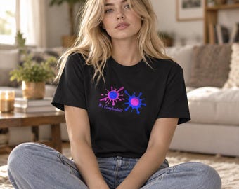 May include: A black short-sleeved t-shirt featuring two colorful paint splatters in pink and blue. The design includes the text It's Complicated! written in a purple script font positioned between the two circular paint splashes.