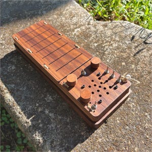 May include: A rectangular wooden sensory board featuring a dark brown finish with a series of parallel horizontal grooves. The surface includes three round wooden knobs, four metal toggle switches, and a grid of small circular holes.