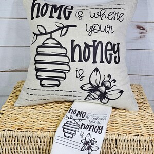 May include: A white pillow with black text that reads "Home is where your honey is". The pillow features a black and white illustration of a honeycomb and a bee.