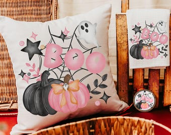 May include: A white pillow with a pink and black Halloween design. The pillow features a spiderweb, a ghost, pumpkins, and the word "BOO" in pink letters.