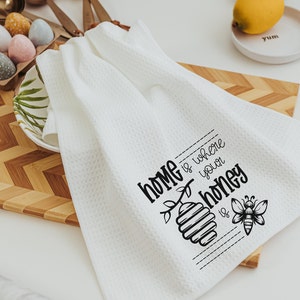 May include: White kitchen towel with black text that reads "Home is where your honey is" with a bee and honeycomb illustration.