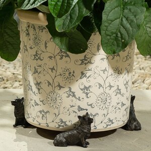 May include: A white ceramic planter with a floral pattern and four black metal dog figurines surrounding the base.