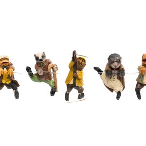 May include: A whimsical collection of five animal figurines, each dressed in vintage attire and suspended from a thin wire. The characters include a frog, badger, otter, and a bear, all with detailed clothing and expressions.