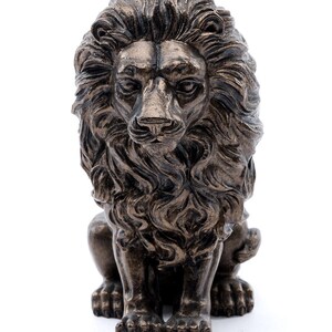 May include: A bronze lion statue with a detailed mane and a seated pose. The lion has a serious expression and is looking straight ahead.
