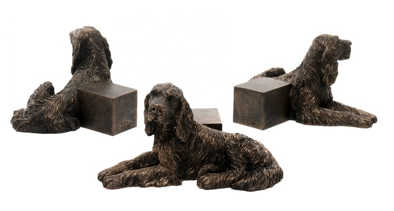 May include: Set of three bronze dog bookends featuring a reclining Cocker Spaniel. Each bookend is approximately 6 inches tall and 4 inches wide.