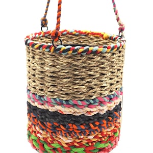 Könnte beinhalten: Ein Hängekorb aus natürlichen geflochtenen Fasern mit einem bunten geflochtenen Seilbesatz. Der Korb hat oben einen schwarzen Metallring zum Aufhängen.