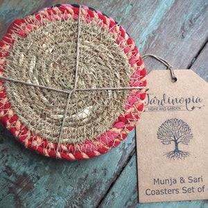 May include: Set of four round woven coasters with red and pink trim. The coasters are made of natural fibers and are tied together with twine. The coasters are labeled "Munjia & Sari Coasters Set of 4" and "Jardಿನopia Home and Garden".