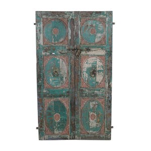 May include: Weathered wooden doors, painted in distressed teal and pink, featuring circular patterns and metal handles. The doors are secured with a metal latch. The doors are a decorative item, with each panel showing signs of age.