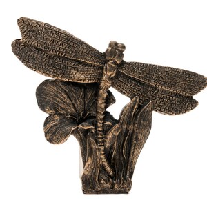 Puede incluir: Una escultura de lib&eacute;lula de color bronce con alas detalladas posada sobre una flor con hojas. La escultura est&aacute; hecha de un material texturizado y tiene un aspecto realista.