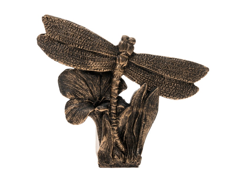 Puede incluir: Una escultura de lib&eacute;lula de color bronce con alas detalladas posada sobre una flor con hojas. La escultura est&aacute; hecha de un material texturizado y tiene un aspecto realista.