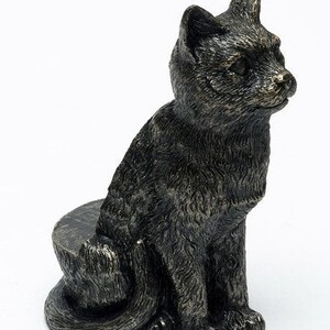 May include: A black cat figurine with a textured finish, sitting on a round base. The cat is looking to the right and has a detailed face.