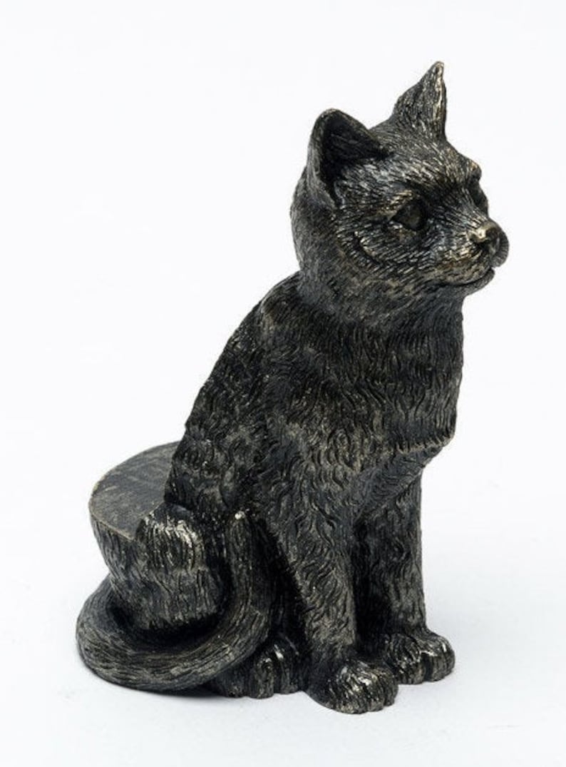 May include: A black cat figurine with a textured finish, sitting on a round base. The cat is looking to the right and has a detailed face.
