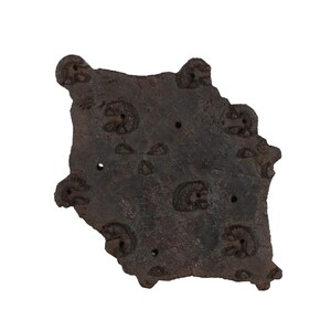Könnte beinhalten: Ein dunkelbrauner Holzblock mit einem geschnitzten Design. Der Block hat eine raue, strukturierte Oberfläche und ist diamantförmig. Er hat mehrere kleine Löcher, die hineingebohrt wurden.