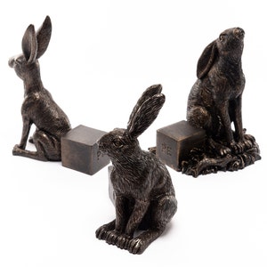 Può includere: Tre sculture di conigli in bronzo, ciascuna seduta su una piccola base quadrata. I conigli sono in pose diverse, uno guarda in alto, uno guarda di lato e uno guarda in basso. Le basi sono incise con le lettere "PF".