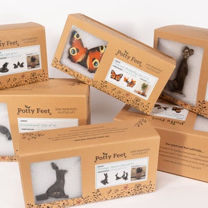 May include: Assortment of cardboard boxes with the text "Potty Feet" printed on them. The boxes contain various animal and butterfly figurines, designed to be used as plant pot feet. The boxes are stacked on top of each other, with the text "Give your pots a little lift" printed on the front of each box.