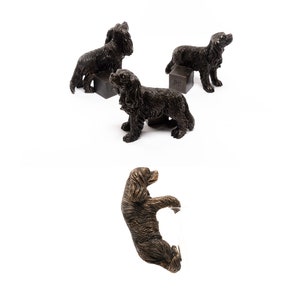 May include: Four bronze figurines of Cavalier King Charles Spaniels in various poses. The figurines are all in a similar style and are detailed with realistic features.