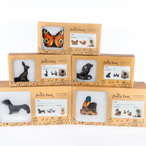Puede incluir: Seis cajas diferentes de pies para macetas, cada una con un dise&ntilde;o de animal diferente. Las cajas est&aacute;n apiladas en forma de pir&aacute;mide. Los animales incluyen una mariposa, un conejo, una foca, un dachshund, un mart&iacute;n pescador y una mariposa. Las cajas son todas marrones y tienen las palabras "Potty Feet" impresas en ellas.