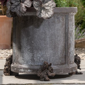 May include: A large, round, gray planter with a distressed finish. The planter is decorated with three squirrel figurines, each with a bushy tail and a playful pose.