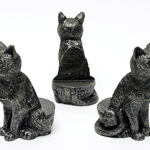 May include: Three black cat bookends with a textured finish. The bookends are in a sitting position with their tails curled around their legs. The middle bookend is facing forward, while the other two are facing sideways. The middle bookend has the letters "PF" engraved on the base.