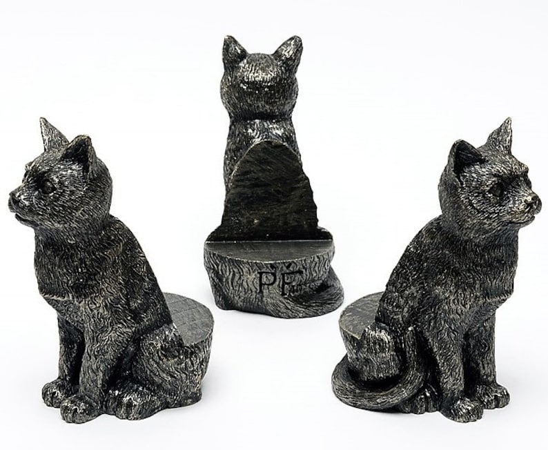 May include: Three black cat bookends with a textured finish. The bookends are in a sitting position with their tails curled around their legs. The middle bookend is facing forward, while the other two are facing sideways. The middle bookend has the letters "PF" engraved on the base.