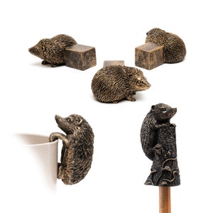 May include: Set of four bronze hedgehog figurines. Three hedgehogs are perched on small square bases, while the fourth is holding onto a mug. The hedgehogs are detailed with textured fur and realistic features.