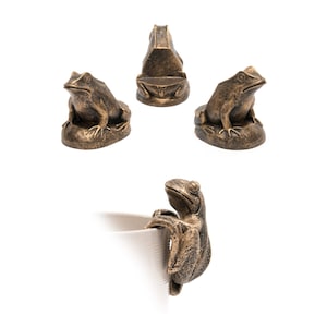 May include: Set of four bronze frog figurines. Three frogs are sitting on a base, while the fourth frog is clinging to a surface. The frogs are a dark bronze color with a slightly weathered finish.