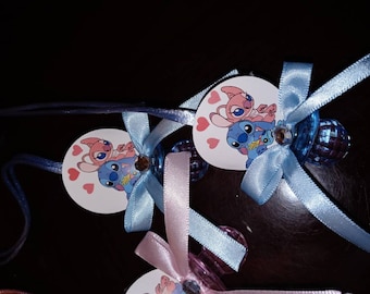 May include: Blue and pink baby shower favors with a blue and pink Stitch and Angel character on a white circle with pink hearts. The favors are attached to a blue and pink ribbon and a clear pacifier.