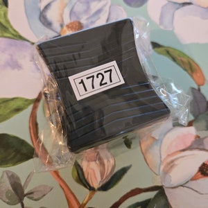 May include: A black plastic object with a label that says "1727" on it. The object is wrapped in clear plastic.