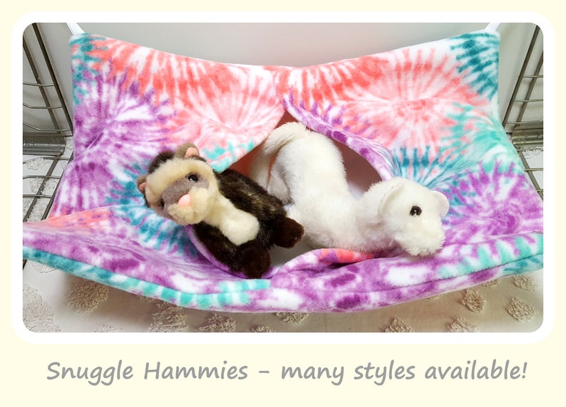 May include: Two stuffed ferrets in a tie-dye hammock. The hammock is purple, pink, and teal with a white background. The text "Snuggle Hammies - many styles available!" is at the bottom of the image.