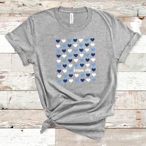 Puede incluir: Camiseta gris con un dise&ntilde;o de corazones azules, blancos y azul claro y el texto "Kansas City".