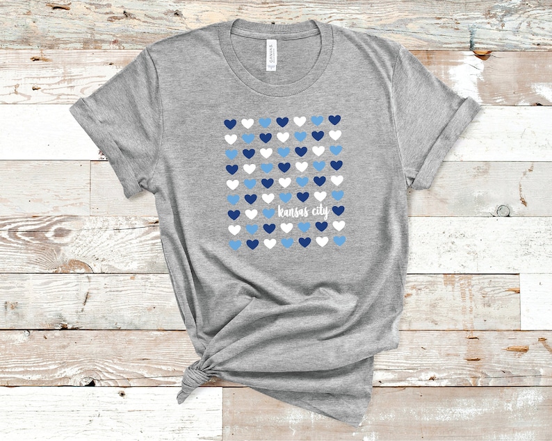 Puede incluir: Camiseta gris con un dise&ntilde;o de corazones azules, blancos y azul claro y el texto "Kansas City".