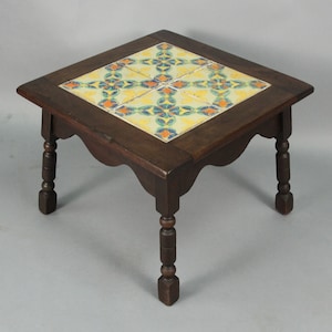 May include: A square wooden table with turned legs and a tiled top. The tile is a geometric pattern of yellow, blue, green, and orange.