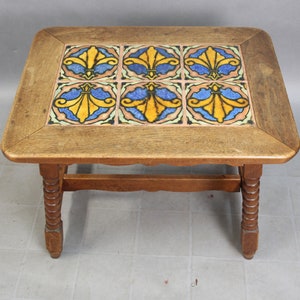 May include: A wooden coffee table with a square top featuring six colorful ceramic tiles with a floral design. The table has a simple, turned leg design.