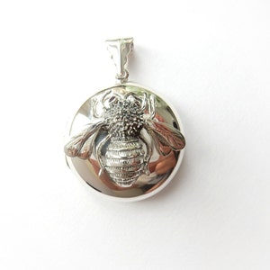 May include: Silver locket pendant featuring a detailed bee design. The locket is round and has a hinged opening.