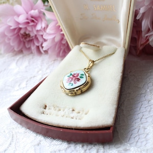 Pode incluir: Um pendente de medalhão oval em tom dourado numa corrente delicada, com uma incrustação de esmalte branco e um motivo floral de rosas cor-de-rosa pintado à mão. O medalhão é exibido numa caixa de joias forrada a veludo creme com o texto H. SAMUEL.