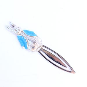 Puede incluir: Marcapáginas plateado con un diseño de conejo con una chaqueta azul. El conejo tiene rasgos faciales detallados y está unido a un marcapáginas largo y delgado. El marcapáginas es de metal y está sobre un fondo blanco.
