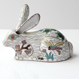 May include: A white cloisonné rabbit figurine with blue, green, yellow, and red floral and butterfly designs.