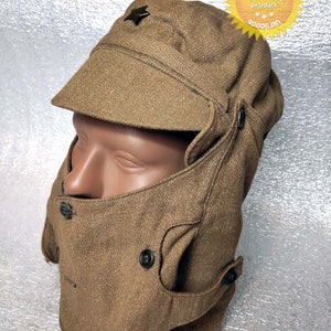 May include: A brown wool winter hat with ear flaps and a chin strap. The hat has a red star on the front and a button on the side.