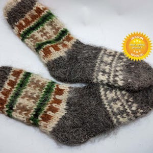 Può includere: Coppia di calzini in lana grigi, marroni, bianchi e verdi con una texture pelosa. I calzini hanno un motivo geometrico.