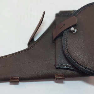 May include: A brown leather holster with a flap and a metal snap. The holster has a stitched design and is in good condition.