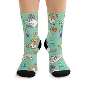 May include: A pair of green socks with a pattern of cats wearing lab coats and holding beakers and test tubes. The socks are black at the toes and heels.