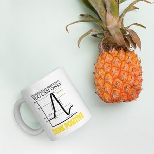 May include: White ceramic mug with a black line graph and the text "Technically speaking, you can only think positive" in black and yellow. The mug is sitting on a light blue surface next to a pineapple.
