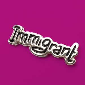 May include: Silver-coloured pin with the word "Immigrant" in black lettering.
