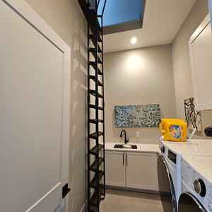 Large attic ladder with custom dark brown stained wooden treads placed in a residential laundry room